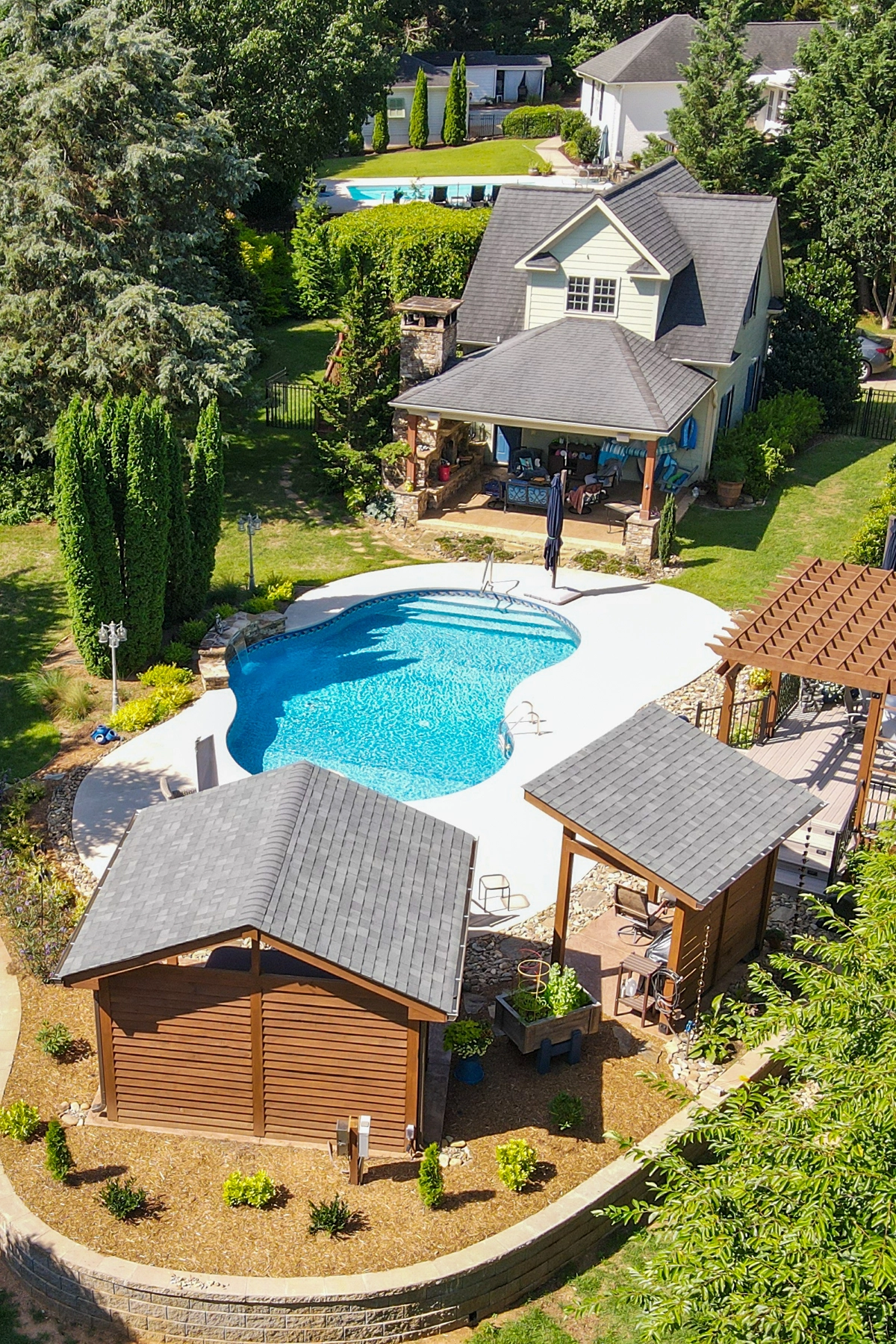 Before and after aerial comparison of outdoor living renovation in Greenville, SC showing expanded deck, pergola, and hardscaping