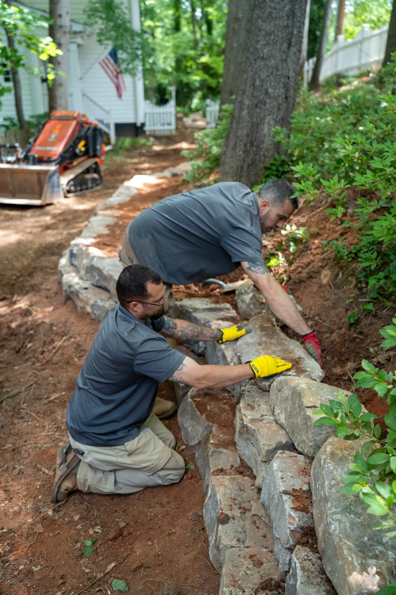 Greenville Outdoor Living crew carefully placing natural stone for a multi-tier retaining wall on a wooded Greenville estate