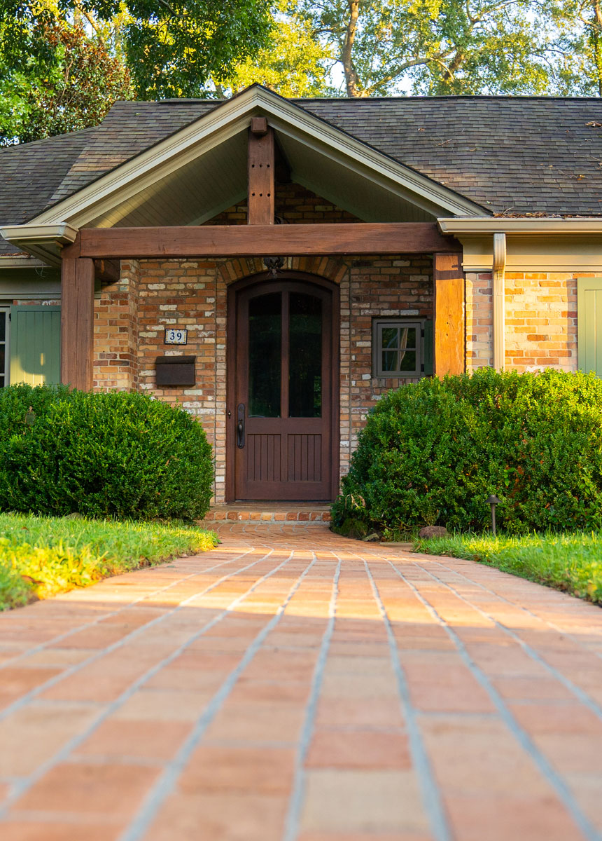 Brick entry walkway and welcoming front porch in a Greenville hardscape project, featuring warm brick detailing and lush foundation plantings