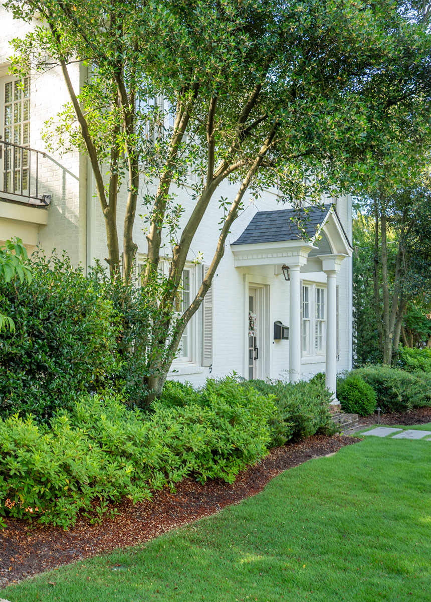 Landscape design Greenville SC example featuring a refined white brick entry with elegant foundation plantings and a welcoming front porch