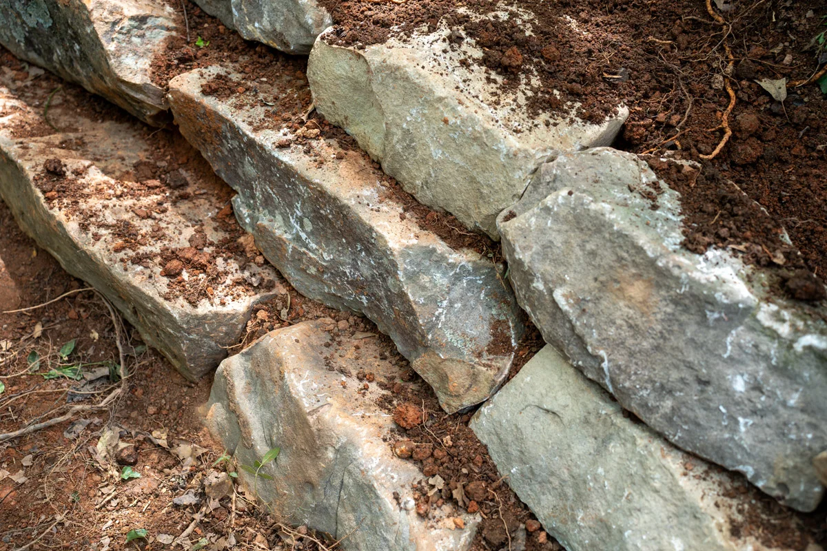 Natural stone retaining wall under construction for a sloped yard in Greenville SC, showing dry-stacked fieldstone and proper drainage base