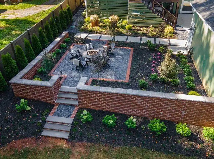 Brick-walled backyard patio with a fire pit and planting beds, an example of design build landscaping in Greenville, SC