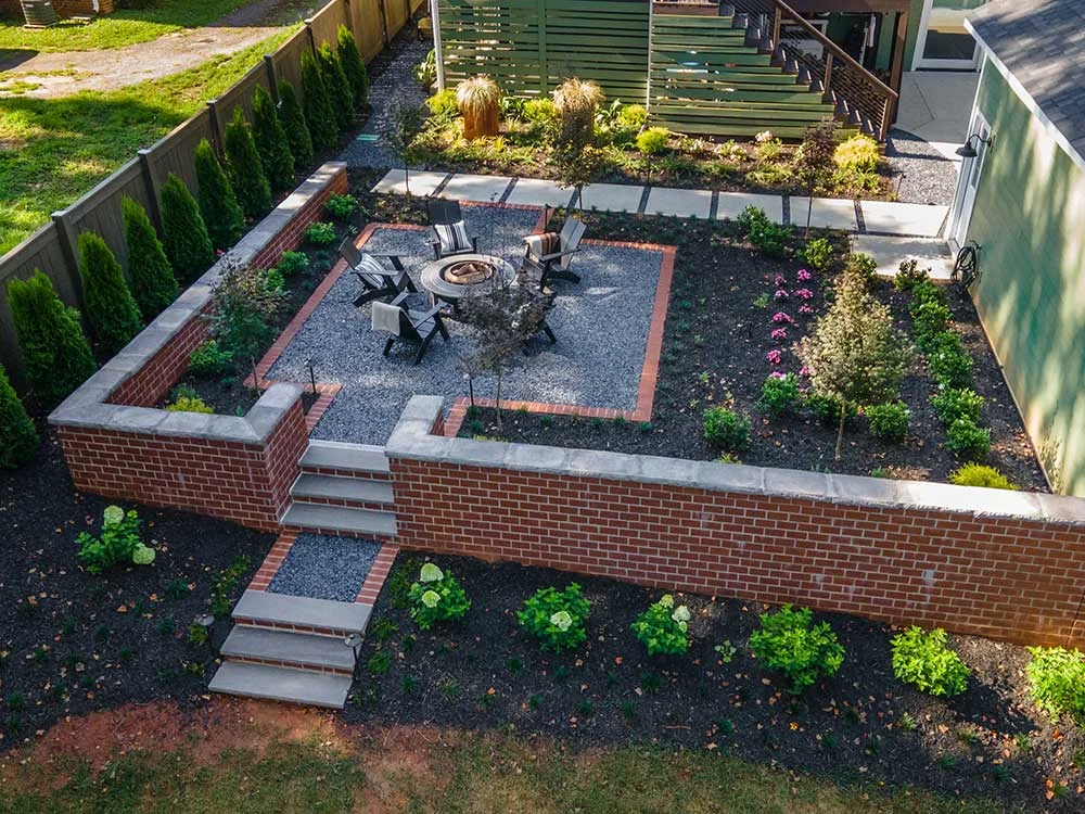 Brick-walled backyard patio with a fire pit and planting beds, an example of design build landscaping in Greenville, SC