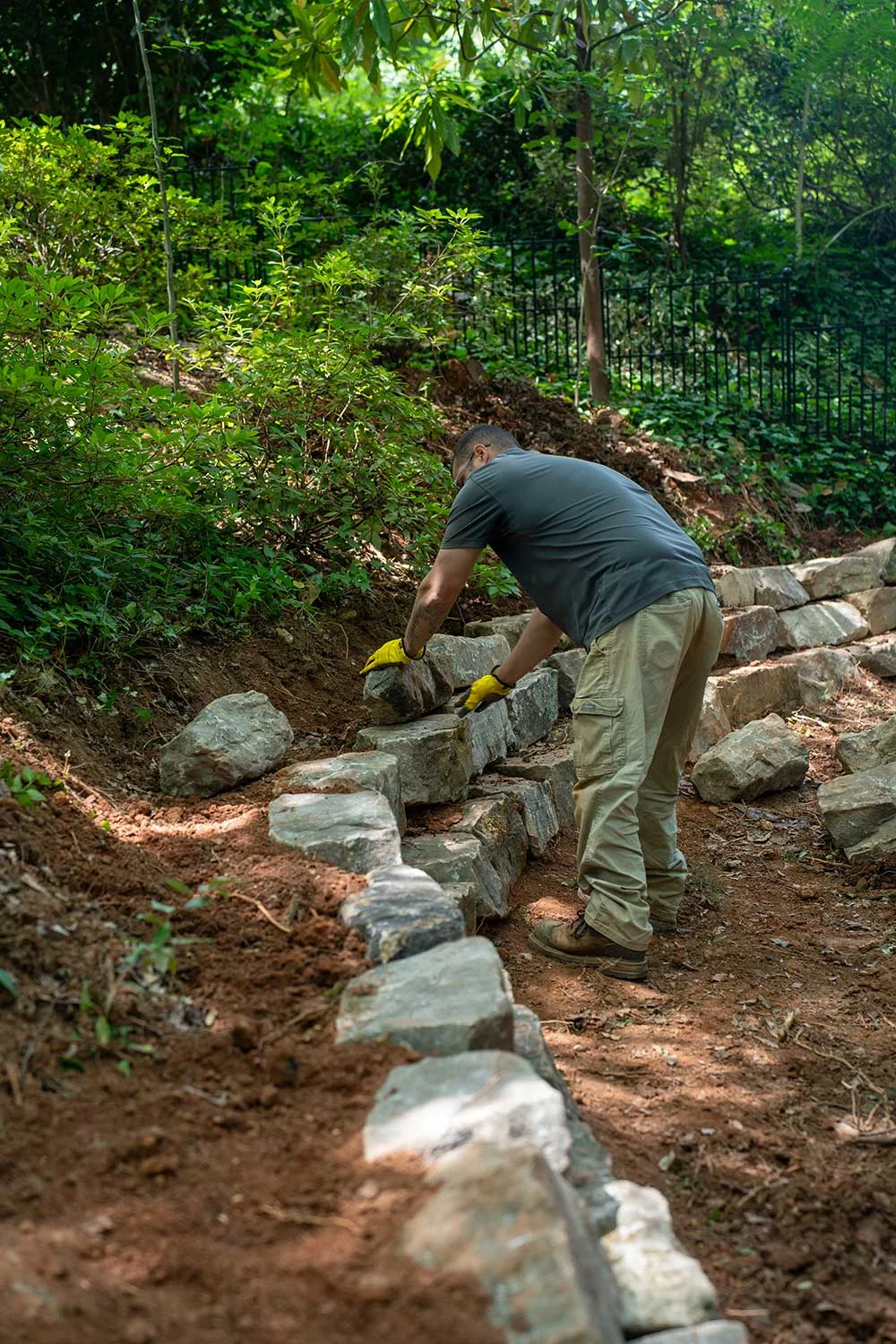 Crew member setting stone for a retaining wall on a wooded slope during design build landscaping in Greenville, SC